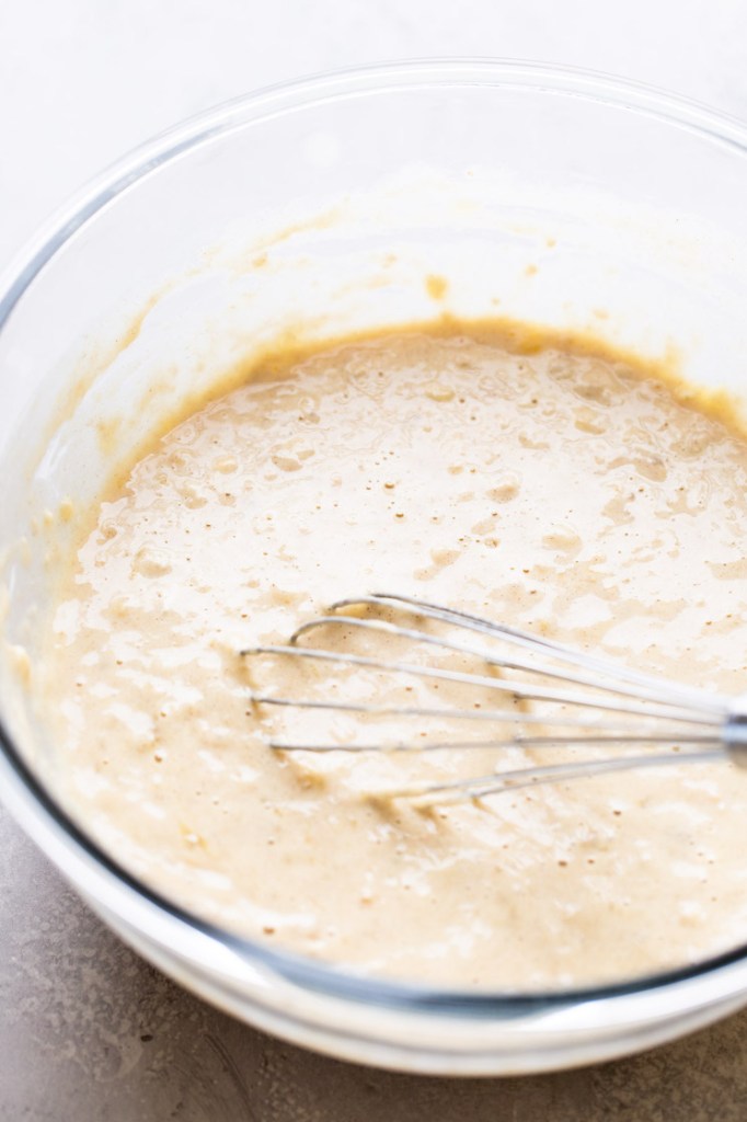 Homemade banana pancake batter with a whisk in a glass mixing bowl. 