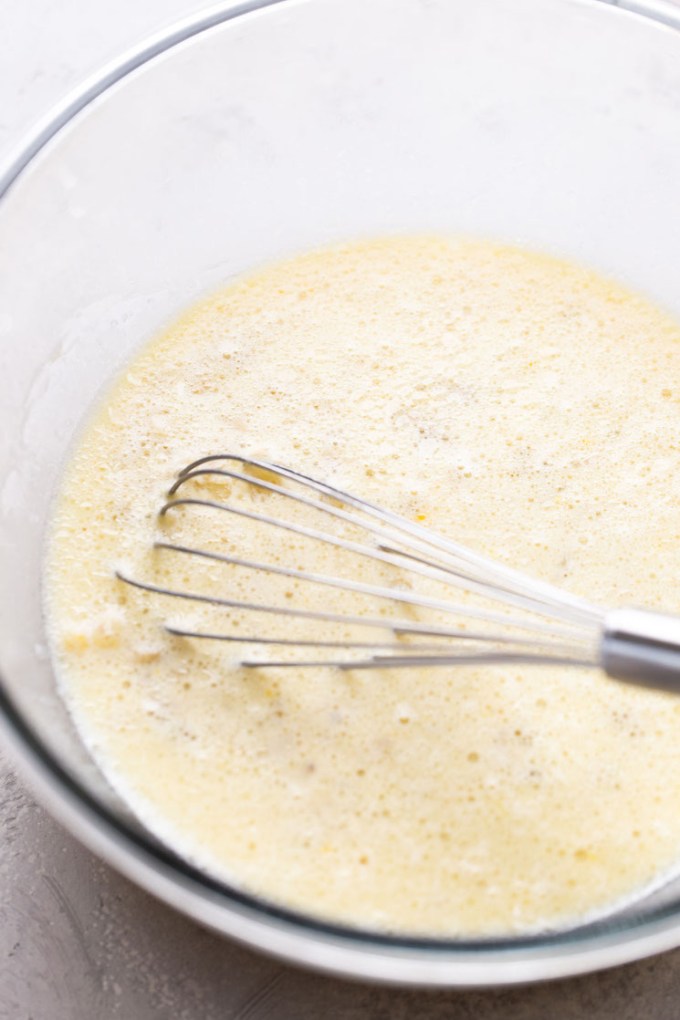 Wet pancake ingredients with a whisk in a glass mixing bowl.