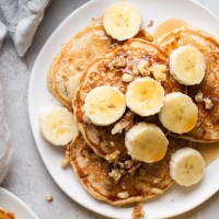 Overhead view of banana pancakes topped with banana slices and chopped walnuts on a white plate.