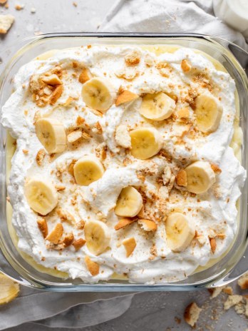 Overhead view of a baking dish filled with banana pudding from scratch. Crushed Nilla Wafers and a banana peel surround the baking dish.