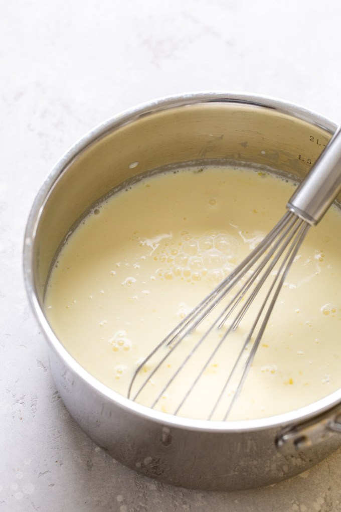 A saucepan filled with vanilla pudding. A whisk rests in the saucepan.