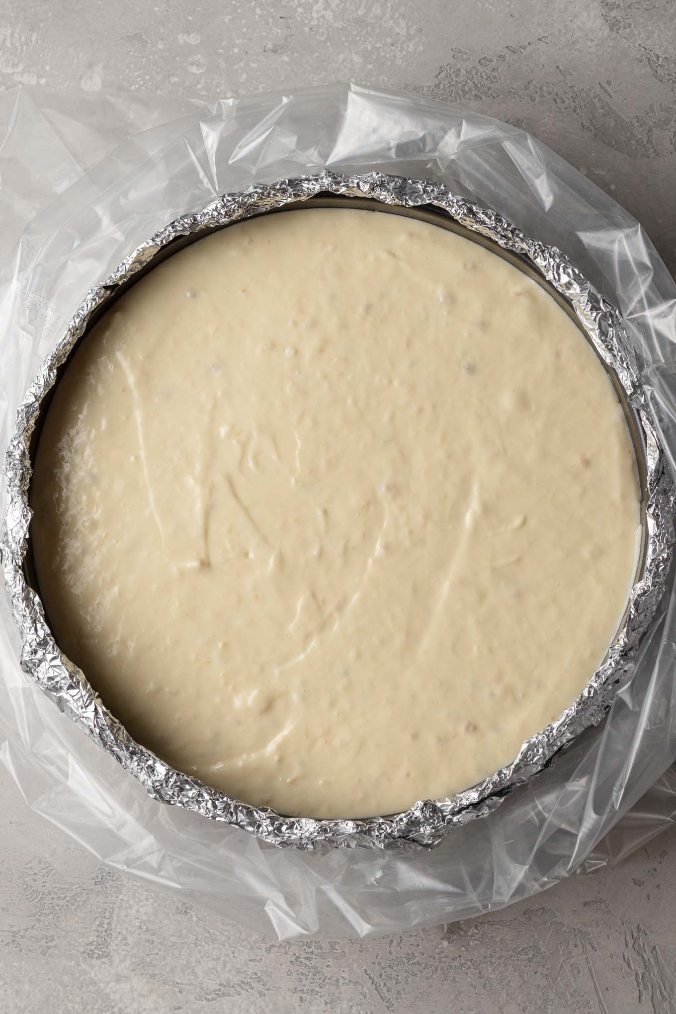 An overhead view of an unbaked cheesecake. The pan is wrapped in foil and placed in an oven bag. 