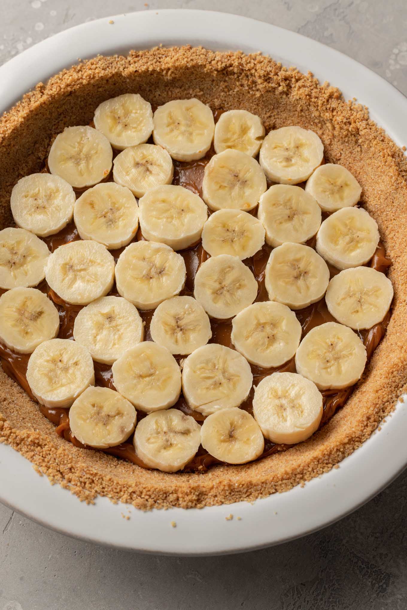 An overhead view of dulce de leche and banana slices layered in a graham cracker crust. 