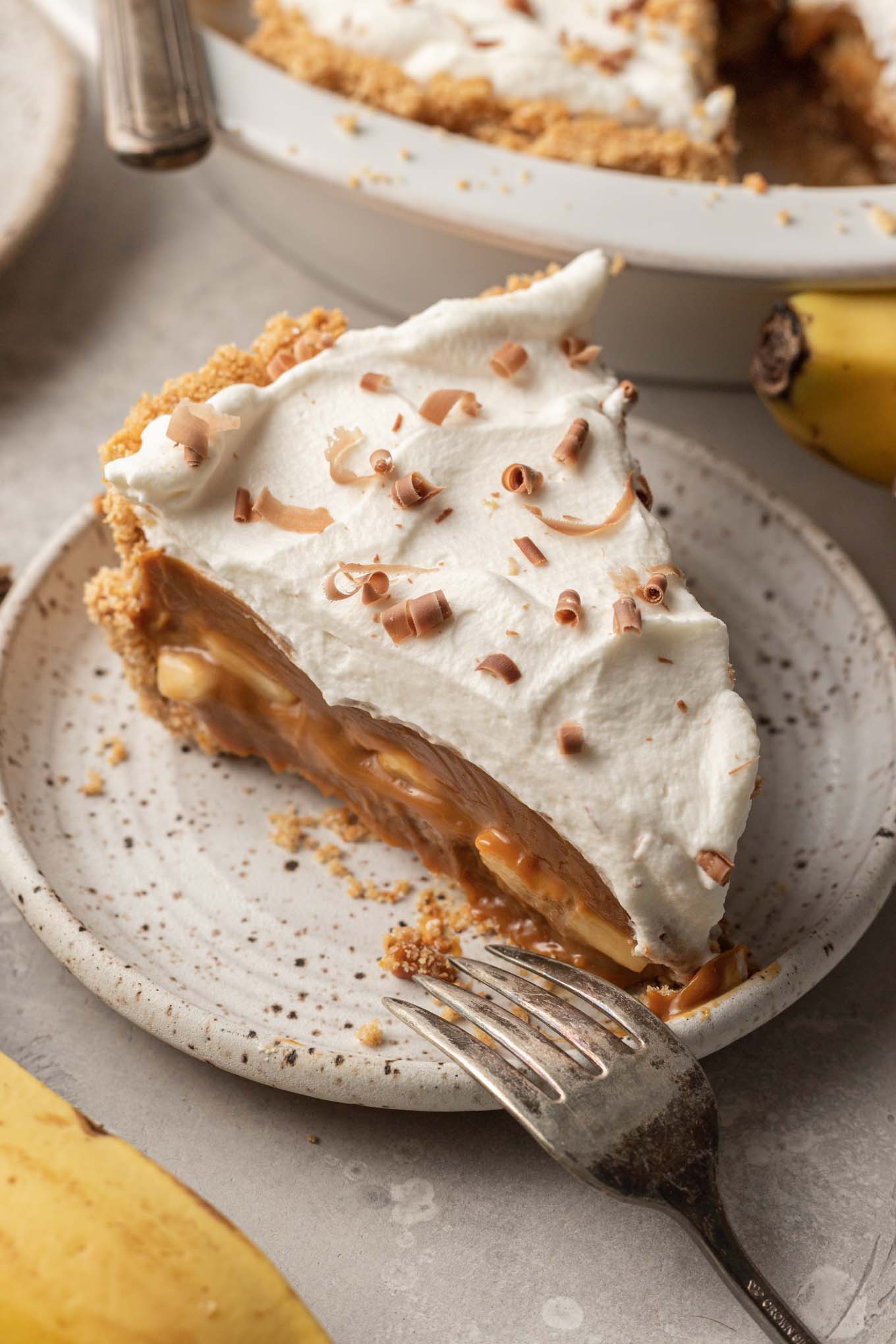 A slice of homemade banoffee pie on a speckled white dessert plate. 