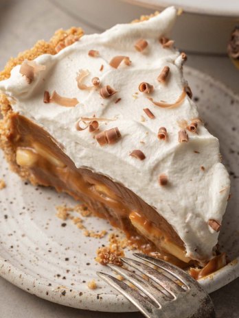 A slice of banoffee pie on a speckled white plate with a fork resting on the side.