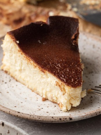 A slice of basque cheesecake on a white speckled plate. A fork is resting on the plate.