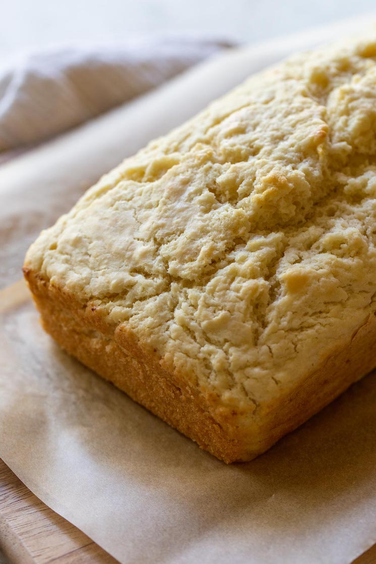 A loaf of beer bread resting on a wood cutting board to cool.