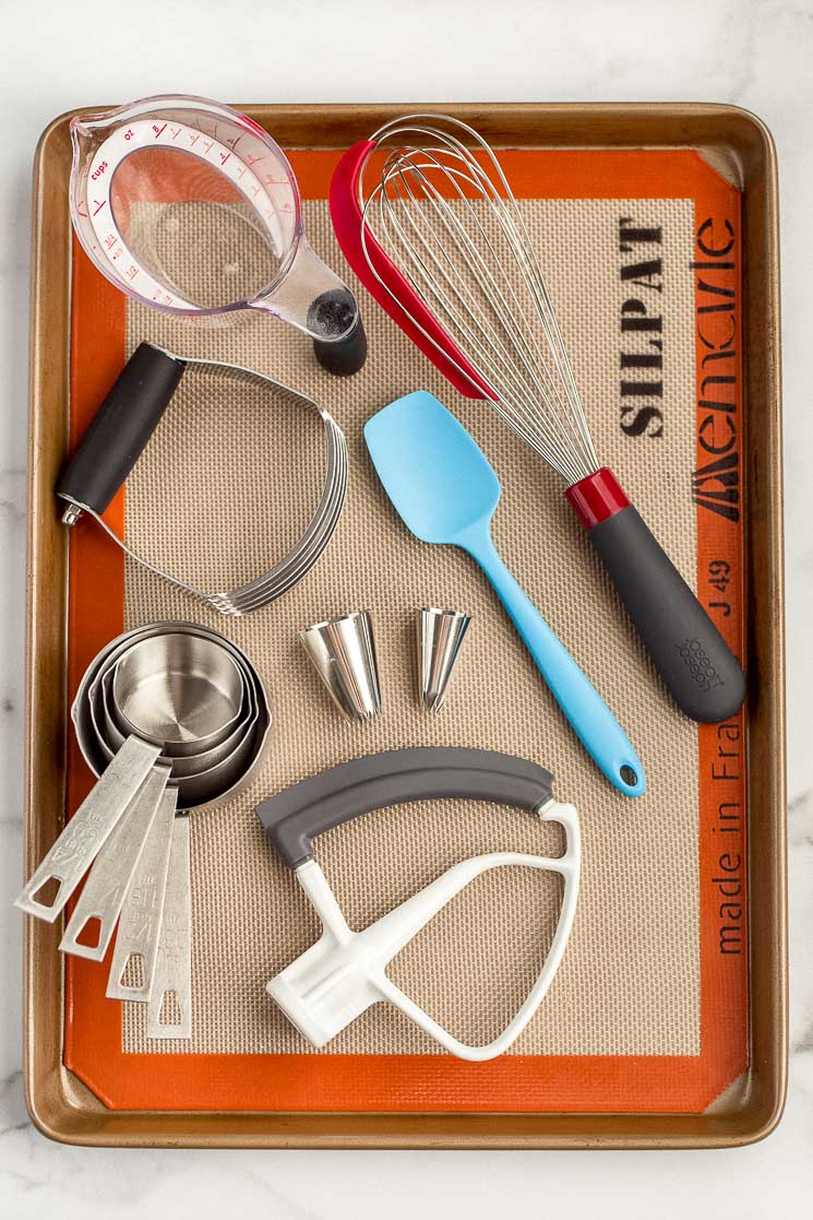 A baking sheet displaying multiple baking tools such as a whisk, measuring cups, and piping tips.