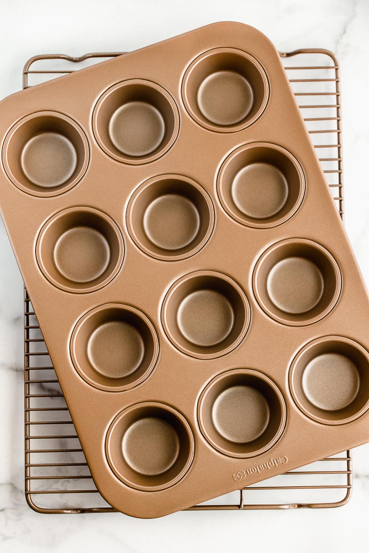 A muffin pan and cooling rack stacked on top of each other on top of a marble surface.