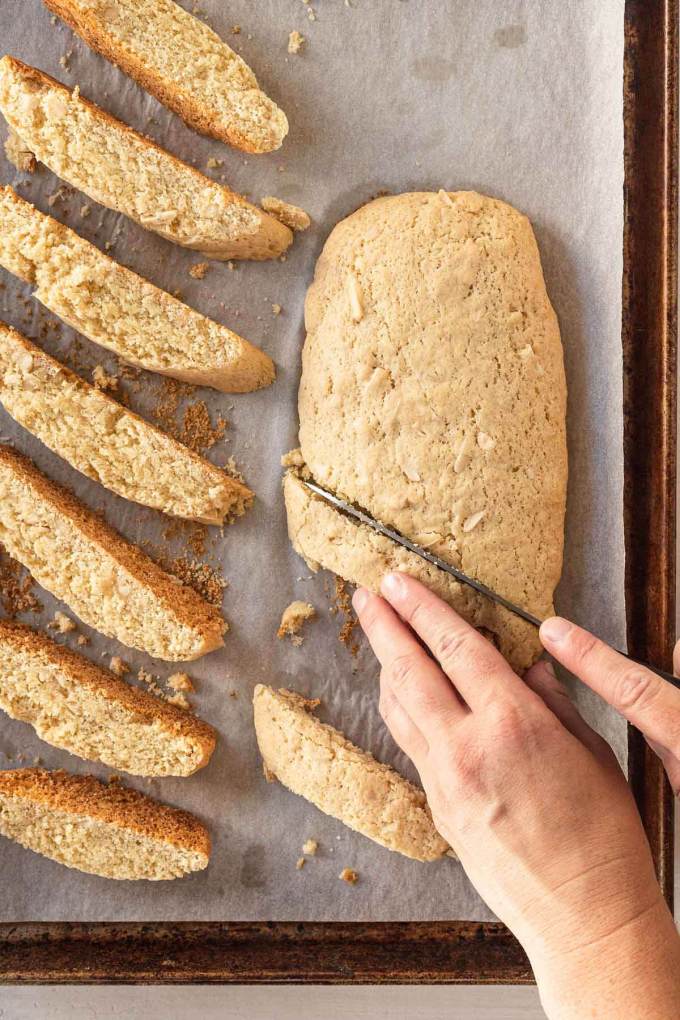 An overhead view of a log of once-baked biscotti being sliced into cookies.