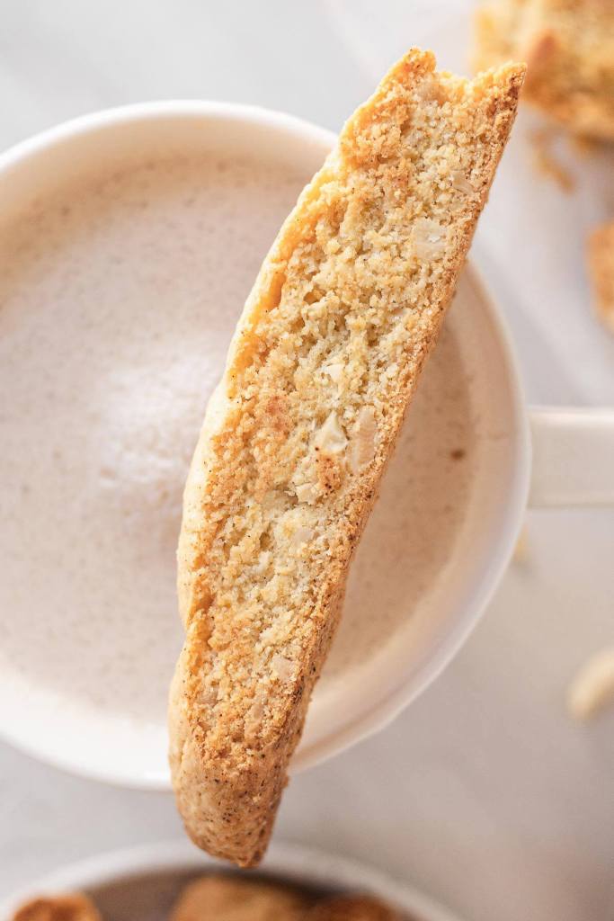 An overhead view of a biscotti cookie resting on the edge of a mug of coffee. 