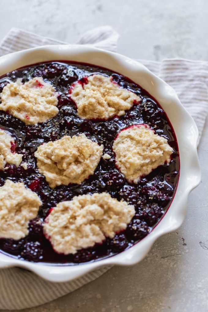 A round baking dish with blackberry filling topped with dollops of biscuit topping.