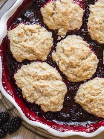 A baked blackberry cobbler in a round white baking dish.