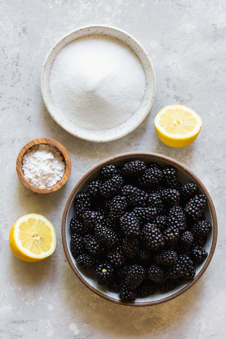 The ingredients for blackberry cobbler filling on a gray surface in rustic bowls.