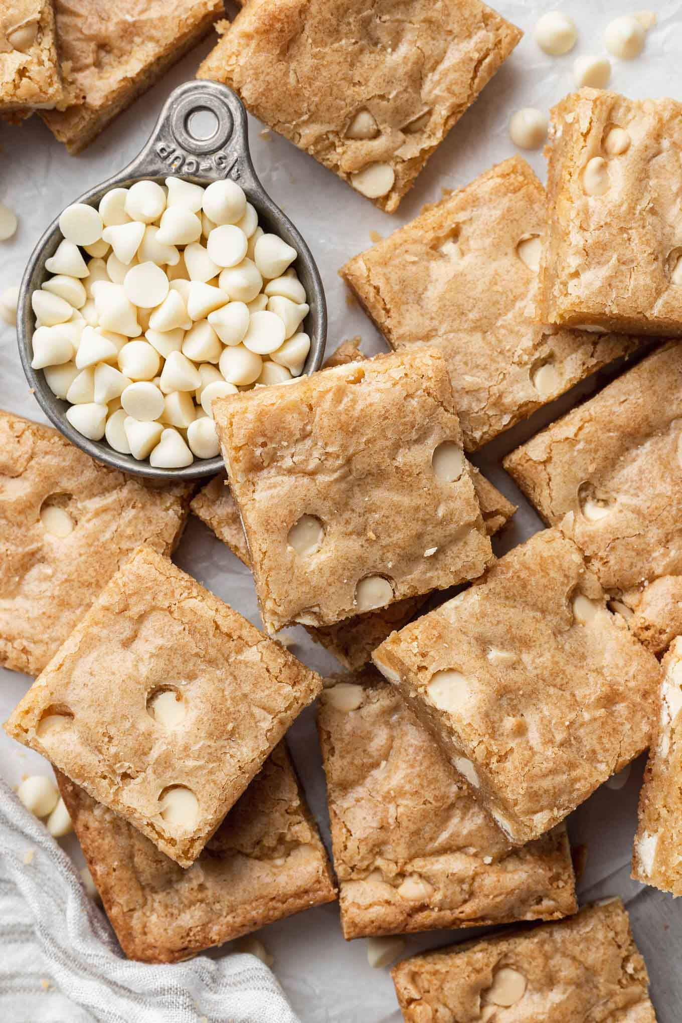 An overhead view of sliced blondies propped up on each other, next to a measuring cup of white chocolate chips. 