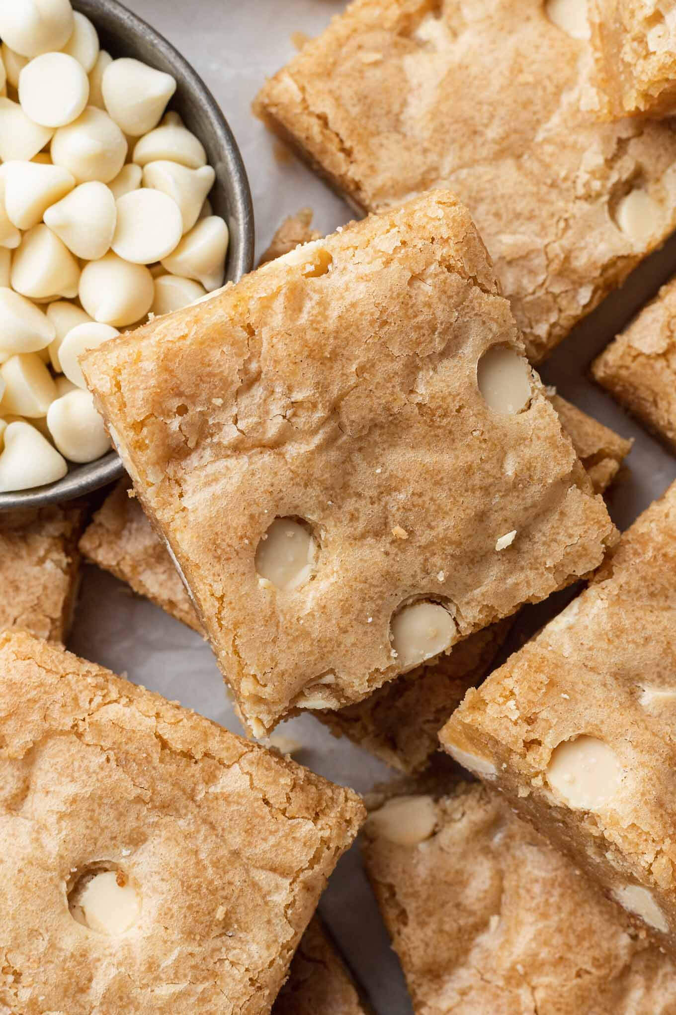 A close-up, overhead view of sliced blondies and a cup of white chocolate chips. 