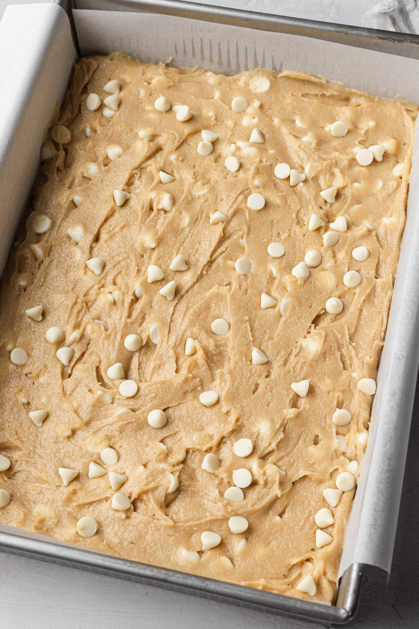 A baking pan lined with parchment paper and filled with blondie batter. 