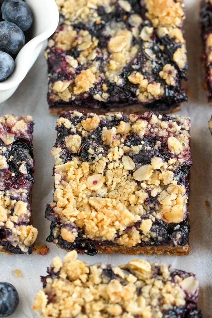 Sliced blueberry bars next to a dish of fresh blueberries. 