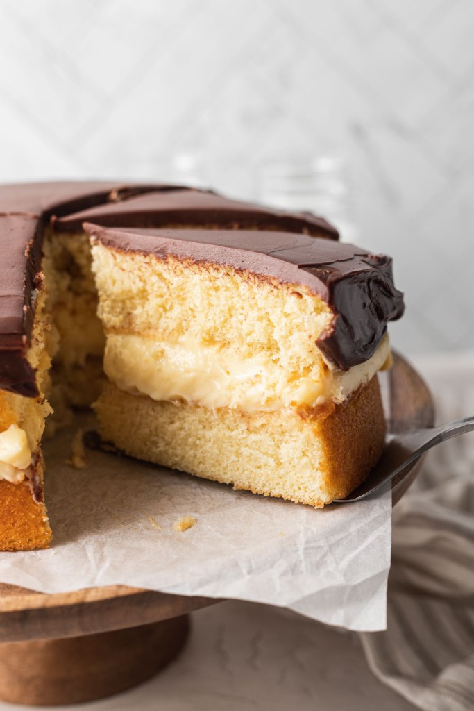 A slice of Boston cream pie being removed from a cake stand. 