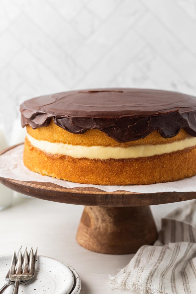 A homemade Boston cream pie on a wooden cake stand. 