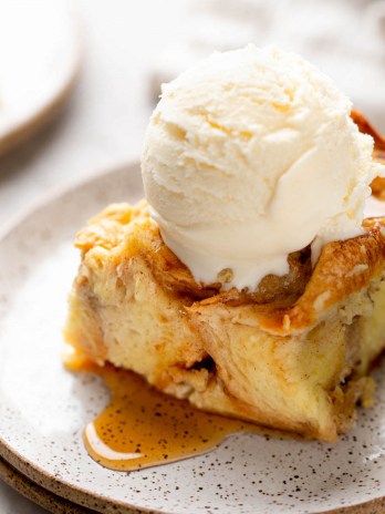 A slice of bread pudding with a scoop of ice cream on top on a white speckled plate.