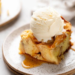A slice of bread pudding with a scoop of ice cream on top on a white speckled plate.