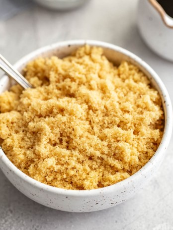 A bowl of light brown sugar with a spoon resting in it. A small container of molasses sits in the background.