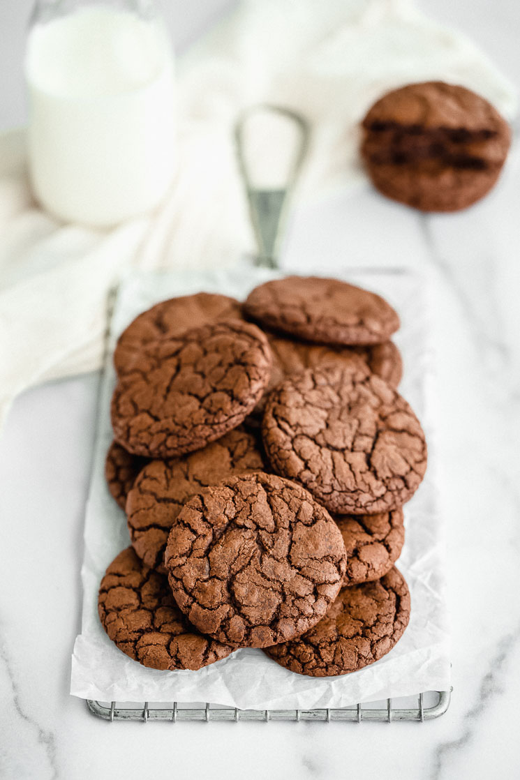 A stack of brownie cookies on top of an antique safety grater with more cookies and milk in the background.