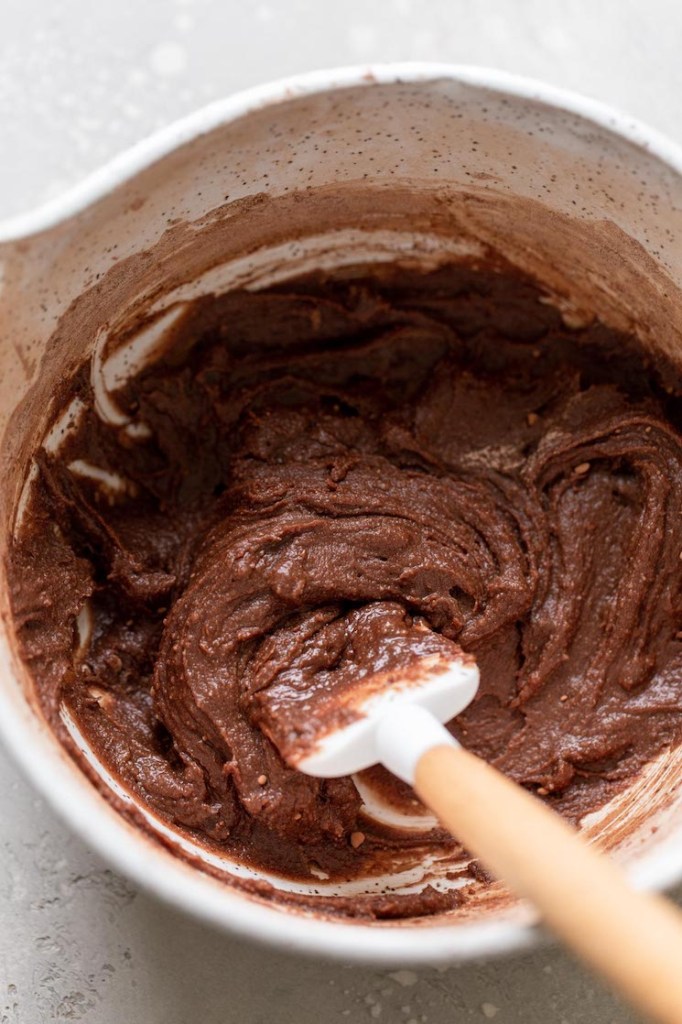 Overhead view of a mixing bowl filled with brownie batter. A rubber spatula is also in the bowl. 