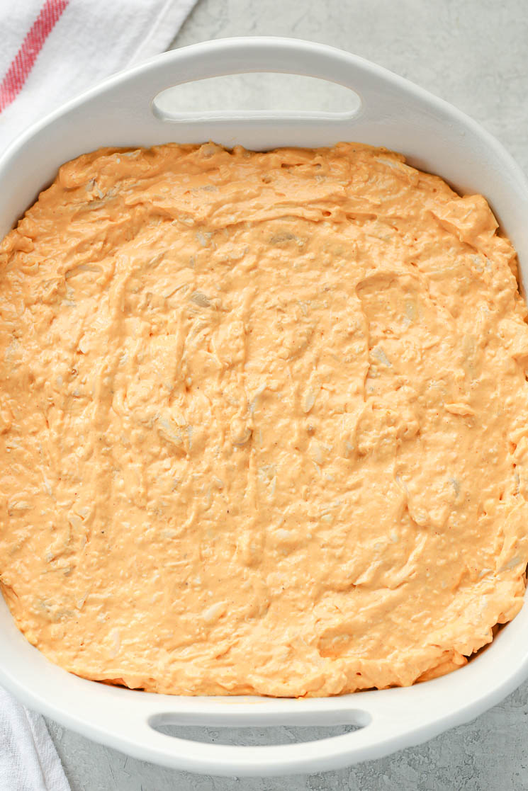 A white 8x8 baking dish filled with creamy buffalo chicken dip and a white napkin on the side. 