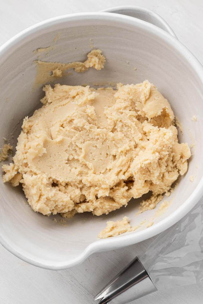 An overhead view of butter cookie dough in a white mixing bowl. 