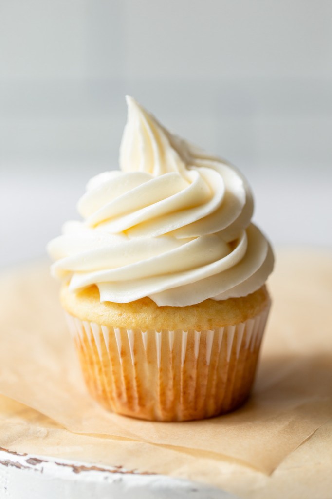 A single cupcake topped with buttercream frosting on top of brown parchment paper.
