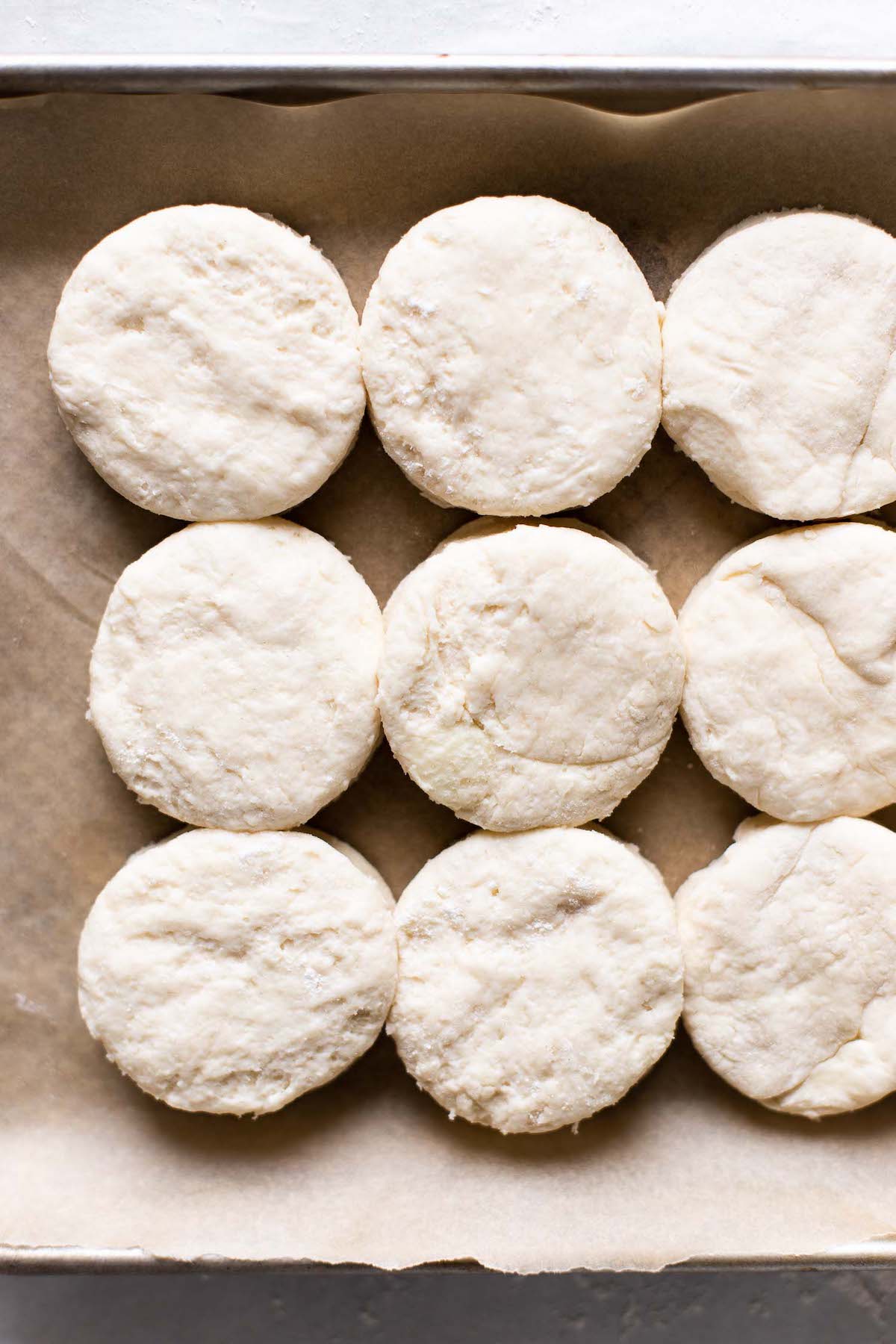 Overhead view of nine raw biscuits on parchment paper.