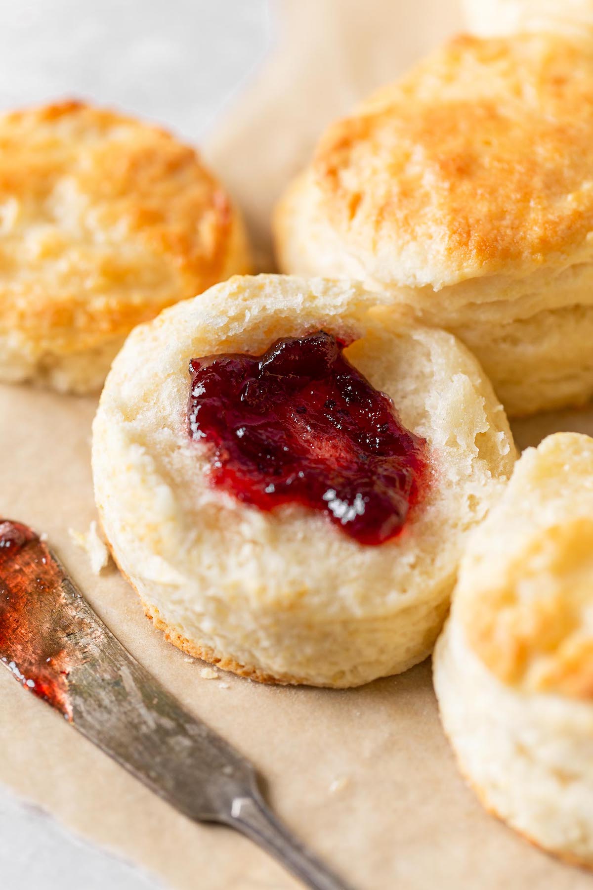 A homemade buttermilk biscuit split in half and topped with jam. More biscuits surround it. 