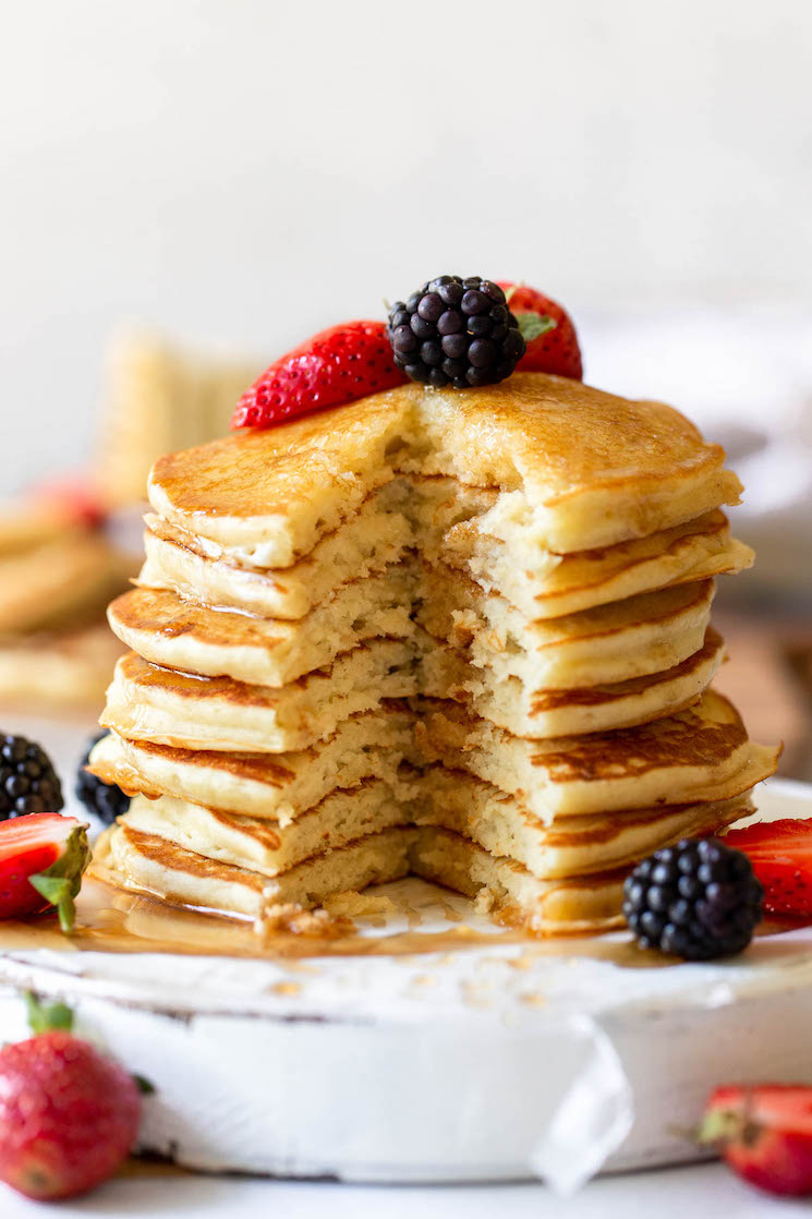 A stack of pancakes topped with syrup and berries and a bite cut out of the whole stack to show the fluffy texture.