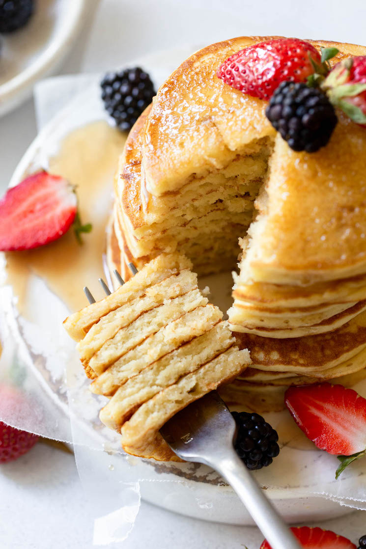 A stack of pancakes topped with berries and syrup with a bite cut out on a fork.