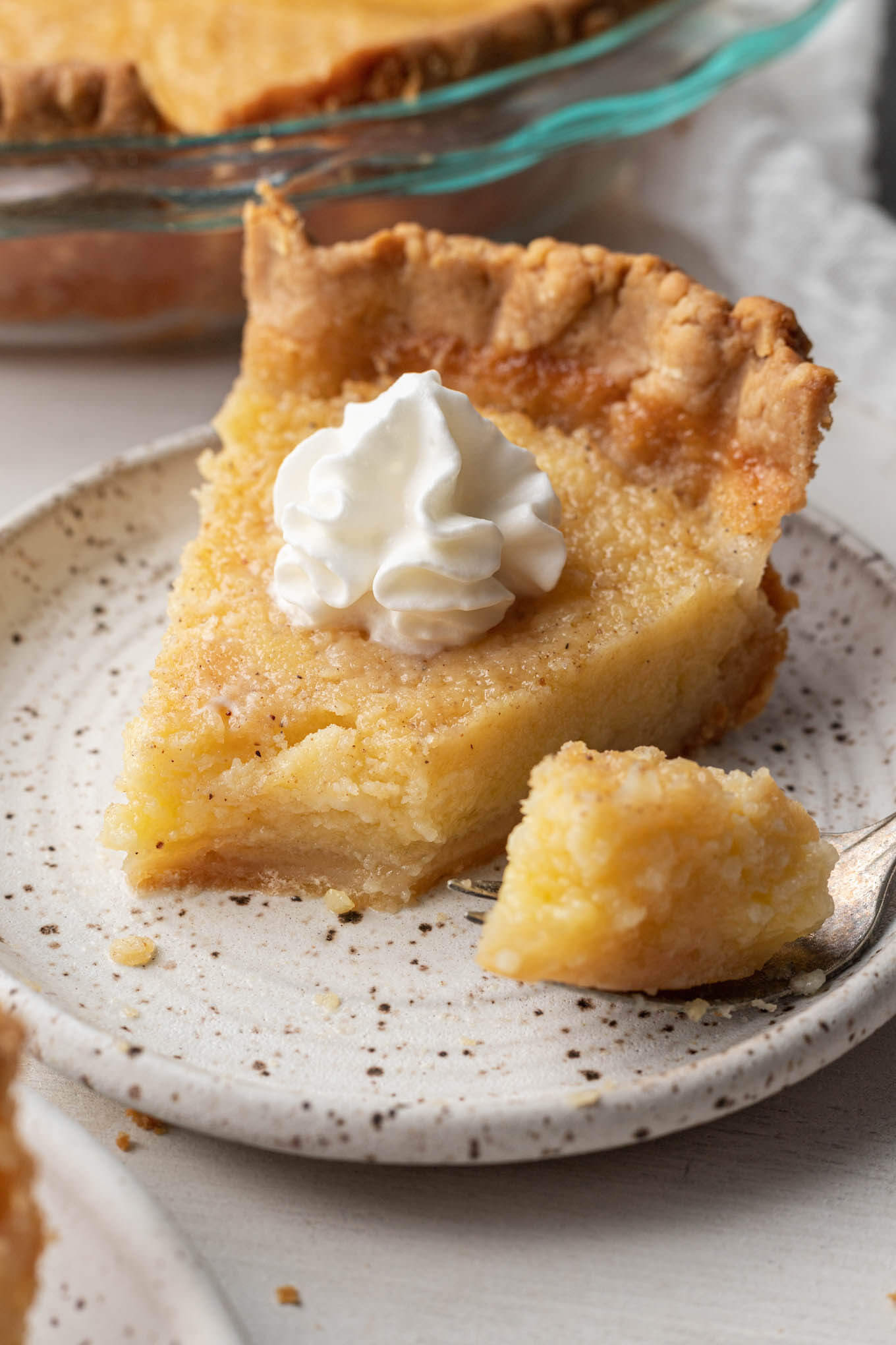 A close-up view of a slice of buttermilk pie, with a bite resting on a fork. 