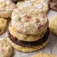 Several different flavors of cake mix cookies stacked on a piece of parchment paper.