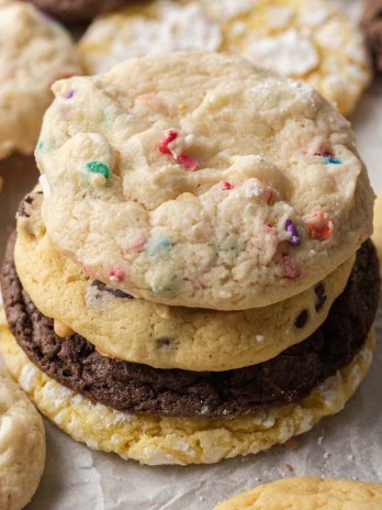 Several different flavors of cake mix cookies stacked on a piece of parchment paper.