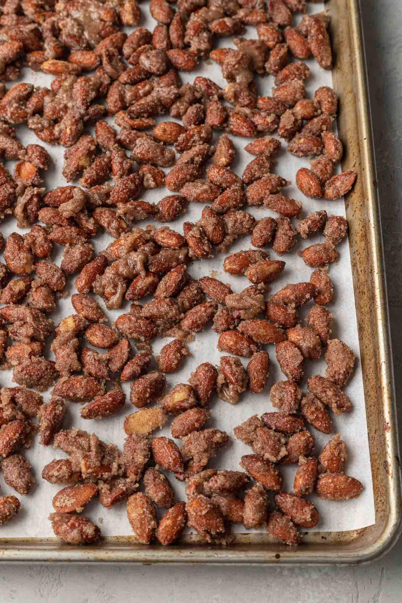 Unbaked candied almonds on a parchment paper lined baking sheet. 