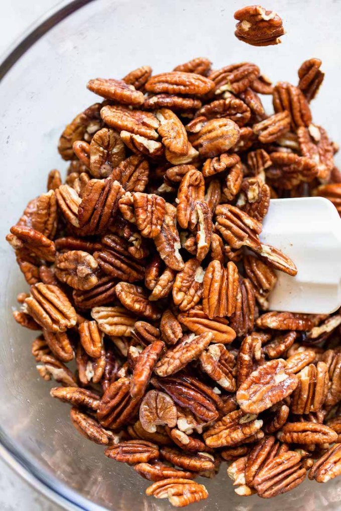 A glass bowl filled with pecan halves being mixed with an egg white mixture.