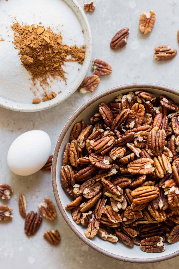 The ingredients needed for candied pecans in different bowls on a gray surface.