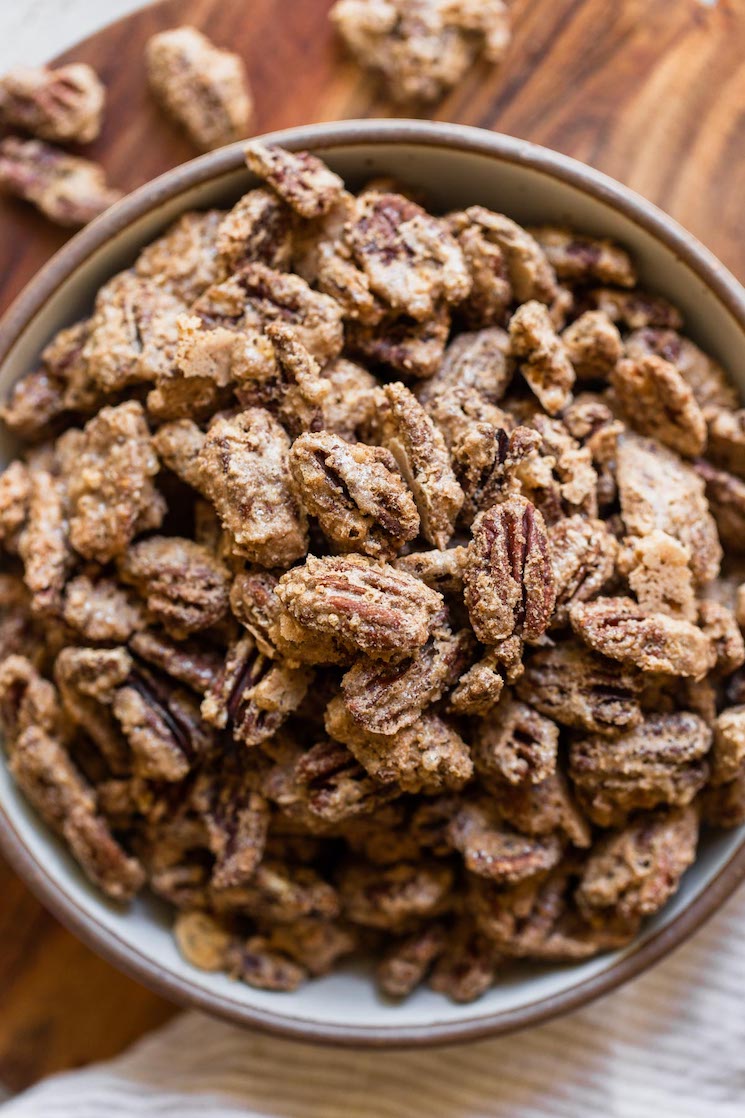 A clay bowl filled with candied pecans resting on top of a wooden tray with a striped linen under the bowl.