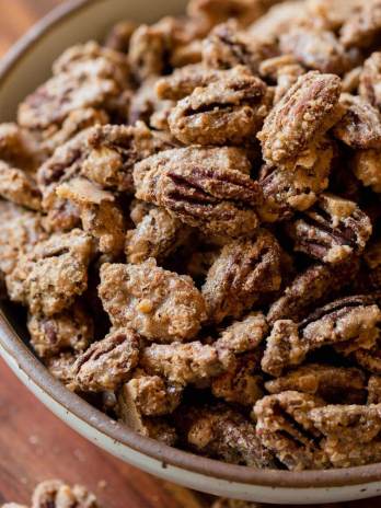 A bowl of candied pecans sitting on a wooden tray.