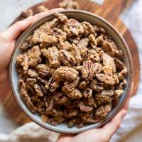 A bowl of candied pecans being held over a wooden surface.