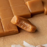 Several sliced caramel candies on a piece of brown parchment paper. One candy has a bite taken out of it.