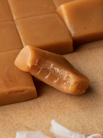 Several sliced caramel candies on a piece of brown parchment paper. One candy has a bite taken out of it.