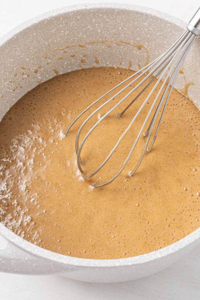 Caramel sauce in a white mixing bowl with a whisk.