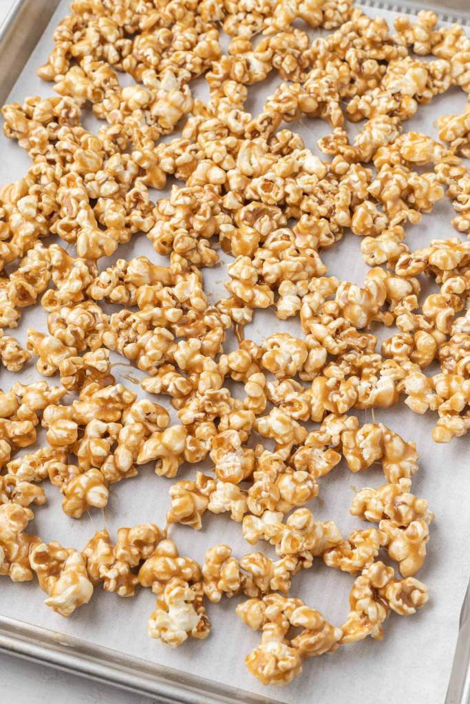 Sticky caramel popcorn on a parchment-lined baking sheet. 