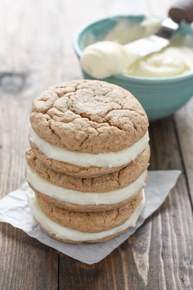 A stack of three carrot cake mix cookies with cream cheese filling. A bow of frosting rests in the background. 